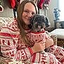 person, dog, pajamas, christmas_stockings, holiday_decor, smiling, indoor, couch, patterned_fabric, fireplace, festive, garland, pet, cute, cozy, matching_outfits, hand_holding, long_hair, brown_hair, window