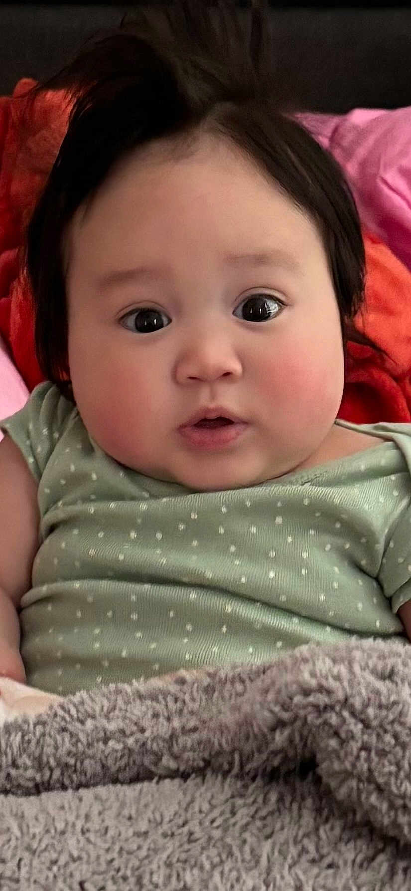 Lilyane Hope joined the competition — help win amazing prizes! baby, infant, face, chubby_cheeks, big_eyes, dark_hair, onesie, green_onesie, polka_dot_pattern, blanket, fleece_blanket, bedding, close_up, portrait, indoors, surprised_expression, adorable, soft_skin, lying_down, cute
