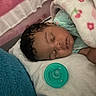 baby, infant, sleeping, peaceful, portrait, face, curly_hair, blanket, crib, pacifier, pink, turquoise, cozy, indoor, nursery, bed, covered, resting, close_up, child