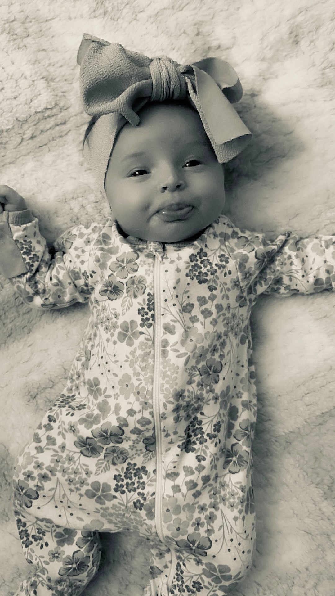 Renesemae Raiyne is registered to the contest to win money with this photo: baby, infant, headband, bow, tongue_out, onesie, floral_pattern, blanket, lying_down, cute, child, smiling, playful, soft_texture, comfortable, portrait, indoors, happy, young, face