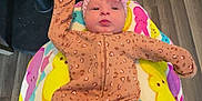Renesemae Raiyne is registered to the contest to win money with this photo: baby, infant, onesie, headband, flower, blanket, bunny_pattern, floor, wooden_floor, chair, black_chair, person, legs, gray_pants, cute, indoors, lying_down, colorful, patterned_blanket, cozy