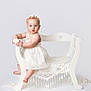 baby, child, flower_crown, white_dress, bench, lace, portrait, studio, cute, infant, smiling, sitting, furniture, decor, innocent, soft_lighting, white_background, pose, curious, young