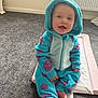 Rosanna is registered to the contest to win money with this photo: baby, child, smiling, hooded_onesie, blue_clothing, purple_spots, carpet, indoor, radiator, changing_mat, sitting, happy, cute, infant, feet, face, portrait, cozy, playtime, young