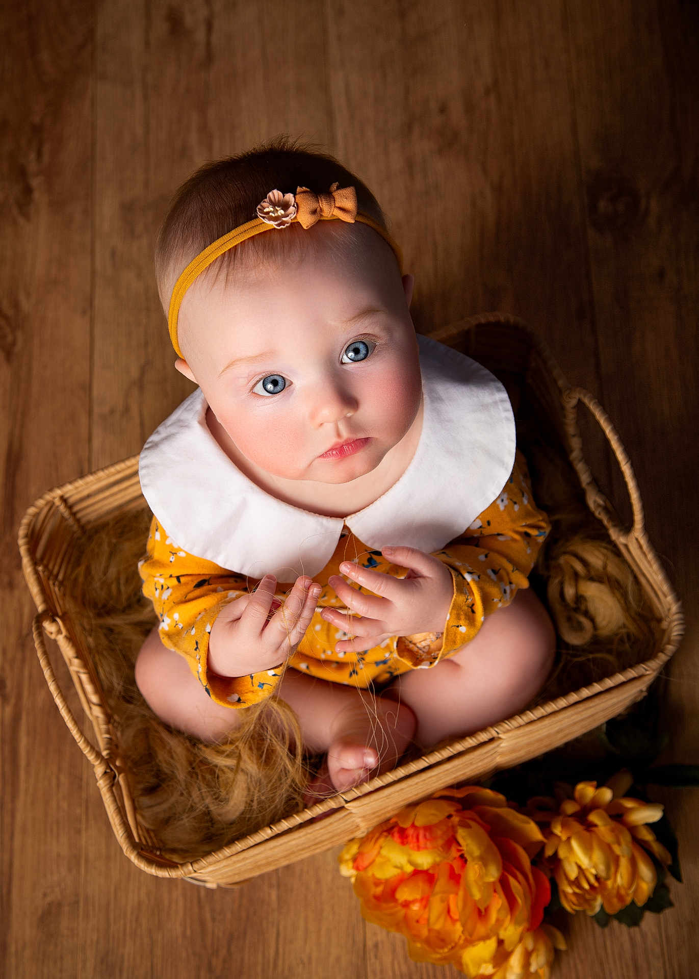 Rosanna joined the competition — help win amazing prizes! baby, infant, child, blue_eyes, headband, basket, wooden_floor, flowers, yellow_clothing, white_collar, hands, feet, cute, portrait, sitting, indoor, soft_lighting, woven_basket, curious, closeup