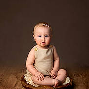 Rosanna joined the competition — help win amazing prizes! baby, child, infant, portrait, sitting, wooden_floor, wooden_bowl, headband, pearl, beige_outfit, studio, neutral_background, cute, curious, indoors, hands, feet, skin, face, blue_eyes