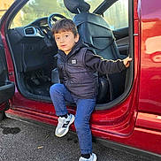 Ilyas a rejoint le concours — aidez-le/la à gagner de superbes lots ! child, boy, car, door, sneakers, clothing, black_vest, blue_pants, outdoor, asphalt, vehicle_interior, seat, curious_expression, casual, daylight, holding_door, young_child, small_person, stepping_out, red_car