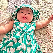 Cattleya is registered to the contest to win money with this photo: baby, child, infant, dress, hat, green, floral_pattern, quilt, blanket, lying_down, cute, chubby_cheeks, soft_lighting, indoors, person, portrait, apparel, headwear, smiling, skin