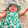 baby, child, infant, dress, hat, green, floral_pattern, quilt, blanket, lying_down, cute, chubby_cheeks, soft_lighting, indoors, person, portrait, apparel, headwear, smiling, skin