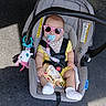 baby, car_seat, sunglasses, pacifier, toy, infant, outdoor, shadow, sunlight, yellow_clothing, white_socks, safety_strap, plush_toy, concrete, bucket, seat, cute, child, casual, wearing