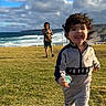 active, casual_clothing, child, cloudy_sky, coast, daytime, fun, grass, happy, jordan, nature, ocean, outdoor, pacifier, playing, running, smiling, toddler, tracksuit, young_child