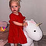 Kahïna participe au concours pour gagner de l'argent avec cette photo : black_shoes, blonde_hair, child, curious, floor, footwear, furniture, girl, hair_buns, indoor, playtime, plush_toy, red_dress, rocking_unicorn, room, standing, toddler, toy, wooden_floor, young_child