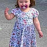 toddler, child, pacifier, dress, floral_pattern, black_socks, bubble, outdoor, concrete, walking, happy, smiling, hair_bow, young_child, person, cute, playful, daylight, casual_clothing, small_child