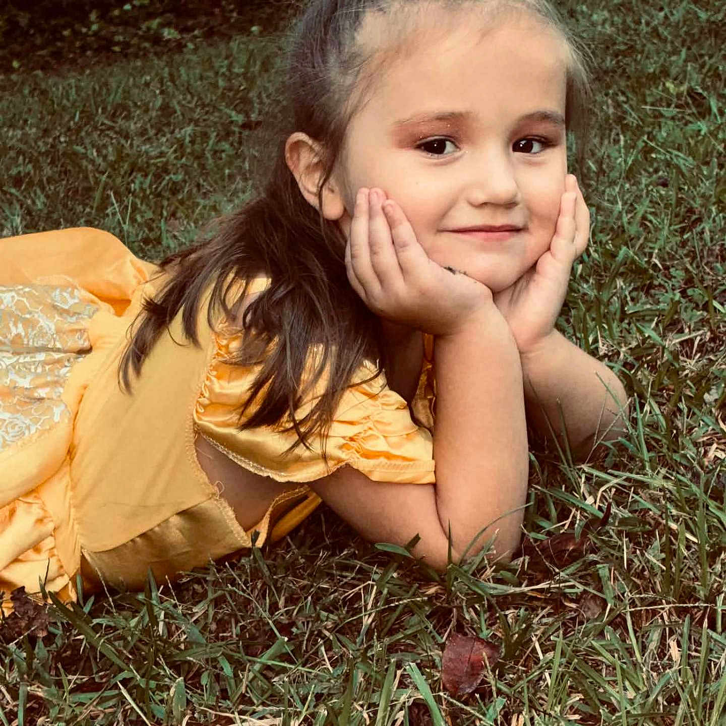 Georgia Deann is registered to the contest to win money with this photo: child, girl, smiling, portrait, outdoor, grass, garden, yellow_dress, hair_bow, long_hair, brown_hair, sitting, lying_down, hands_on_cheeks, face, happy, sunlight, nature, grass_lawn, photography