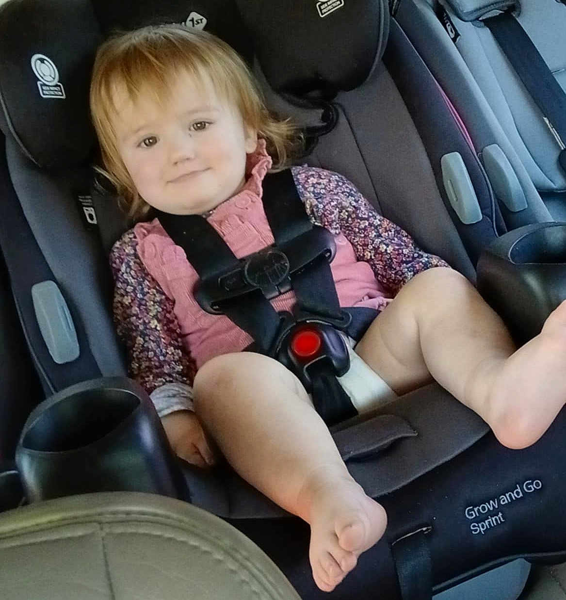 Americus Leighann is registered to the contest to win money with this photo: toddler, child, car_seat, safety_harness, smiling, foot, pink_clothing, floral_pattern, seatbelt, car_interior, baby, cute, strapped_in, portrait, young_child, seat, travel, child_safety, happy, infant