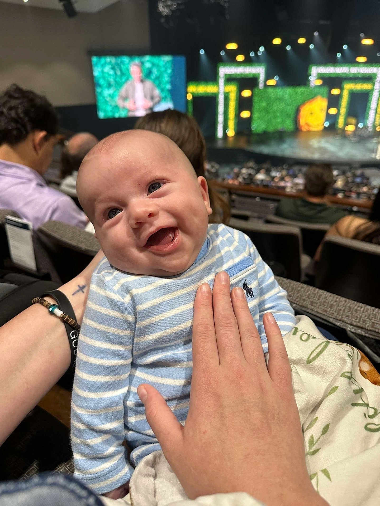 Acen joined the competition — help win amazing prizes! baby, smiling, striped_clothing, blue, infant, hand, auditorium, theater, stage, screen, crowd, seated_people, happy, person, portrait, indoor, blanket, light, event, audience