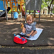 Aaron joined the competition — help win amazing prizes! child, toddler, playground, toy, red_toy, snack, towel, sneakers, outdoor, trees, play_equipment, slide, daylight, smiling, casual_clothing, park, shade, curly_hair, happy, young_child