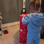 Aaron participe au concours pour gagner de l'argent avec cette photo : back_view, blue_clothing, child, curiosity, curly_hair, door, floor, gift_box, holiday, home, indoor, person, present, red_wrapping_paper, sneakers, tile_floor, tracksuit, unwrapping, wreath, young_child