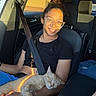 person, cat, car, seatbelt, glasses, black_shirt, orange_cat, sleeping_cat, sunlight, happy, smiling, seat, interior, window, casual, relaxed, portrait, pet, cozy, daylight