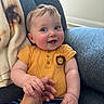 baby, child, smiling, hand_holding, yellow_shirt, lion_patch, striped_pants, blue_chair, blanket, cozy, happy, indoor, portrait, cute, infant, skin, hair, person, seated, playful