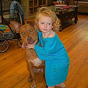 Gianna is registered to the contest to win money with this photo: barefoot, blue_shirt, child, couch, curly_hair, dog, domestic, face, furniture, hug, indoor, laundry_basket, living_room, person, pet, stroller, table, toddler, window, wooden_floor