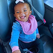 Emerie is registered to the contest to win money with this photo: baby, child, smiling, car_seat, seatbelt, denim_jacket, pink_bib, pink_bow, sneakers, Adidas, black_pants, happy, cute, indoor, portrait, person, footwear, car_interior, safety, young_child