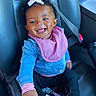baby, child, smiling, car_seat, seatbelt, denim_jacket, pink_bib, pink_bow, sneakers, Adidas, black_pants, happy, cute, indoor, portrait, person, footwear, car_interior, safety, young_child