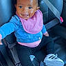 baby, child, car_seat, denim_jacket, pink_bib, pink_bow, sneakers, black_pants, smiling, happy, seatbelt, cute, infant, portrait, person, indoor, car_interior, footwear, reaching_out, young_child