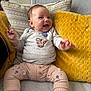 baby, smiling, happy, couch, pillow, yellow_pillow, patterned_pillow, baby_clothes, bear_design, sitting, infant, cute, indoors, child, cozy, plush, hand_gesture, portrait, comfort, soft_furniture