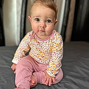 Britton is registered to the contest to win money with this photo: baby, child, infant, sitting, barefoot, pink_pants, floral_shirt, curly_hair, large_eyes, indoor, portrait, soft_light, bed, gray_bedspread, cute, looking_at_camera, young_child, close_up, skin, human