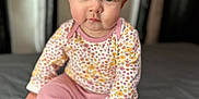 Britton is registered to the contest to win money with this photo: baby, child, infant, sitting, barefoot, pink_pants, floral_shirt, curly_hair, large_eyes, indoor, portrait, soft_light, bed, gray_bedspread, cute, looking_at_camera, young_child, close_up, skin, human