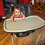 Britton is registered to the contest to win money with this photo: baby, high_chair, food, bib, wooden_floor, kitchen, table, chair, red_wall, curious, child, indoor, person, floor, foot, hand, face, expression, tray, furniture