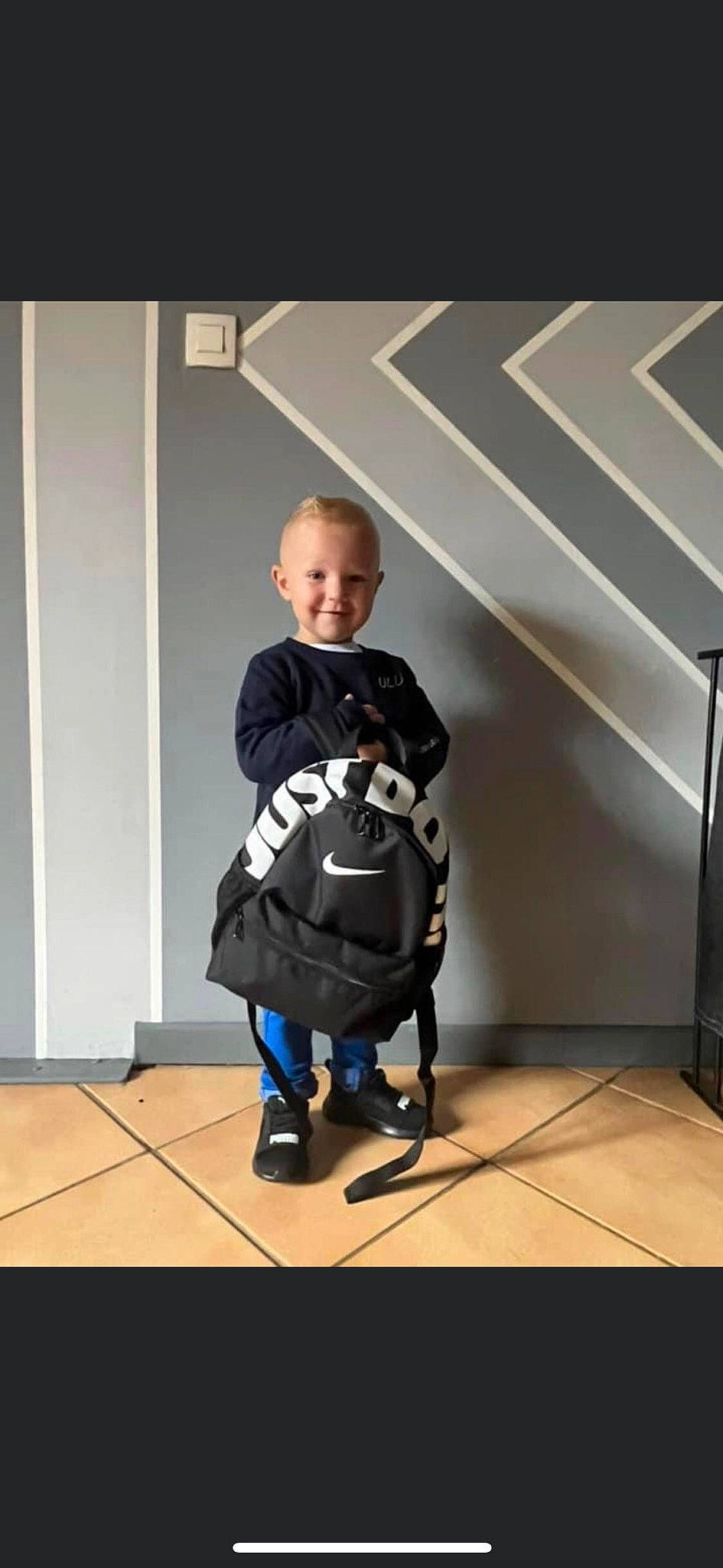 Tiago participe au concours pour gagner de l'argent avec cette photo : baby, baby_products, bag, child, electric_blue, fashion_accessory, floor, flooring, fun, joy, person, personal_protective_equipment, room, shoe, sitting, sleeve, smile, sneakers, standing, t_shirt