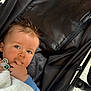 baby, child, pacifier, blanket, stroller, face, hand, blue_clothing, black_fabric, outdoor, closeup, infant, person, cute, portrait, young_child, soft_texture, relaxing, daylight, expression