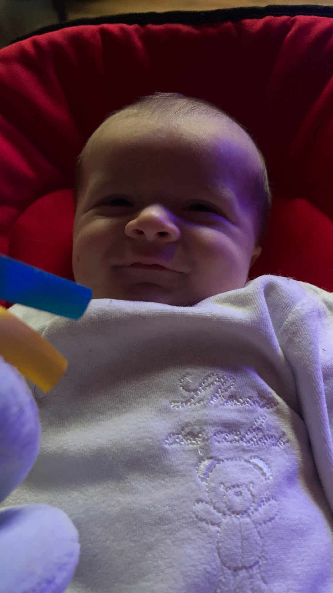 Emrys a rejoint le concours — aidez-le/la à gagner de superbes lots ! baby, infant, smile, face, red_cushion, white_clothing, teddy_bear_embroidery, toy, colorful_toy, hand, close_up, indoor, child, cute, soft_lighting, portrait, young_child, cozy, fabric, person
