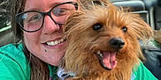 Winnifred Journee is registered to the contest to win money with this photo: animal, bracelet, car_interior, casual, daylight, dog, glasses, green_shirt, happy, holding, jewelry, long_hair, person, pet, portrait, seat, small_dog, smile, tattoo, window