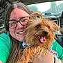 animal, bracelet, car_interior, casual, daylight, dog, glasses, green_shirt, happy, holding, jewelry, long_hair, person, pet, portrait, seat, small_dog, smile, tattoo, window
