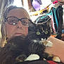 woman, cat, glasses, indoor, furniture, bag, window, curtain, tortoiseshell_cat, pet, face, person, hair, whiskers, eyes, fur, arm, clothing, home, relaxing