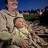 baby, blanket, child, clothing, event, face, family, glasses, grass, happy, night, outdoor, people, portrait, quilt, sitting, smile, trees, warm, woman