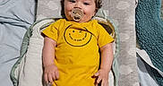 Leonard is registered to the contest to win money with this photo: baby, child, pacifier, yellow_onesie, changing_pad, blanket, bed, infant, cute, smiling, soft_lighting, indoors, resting, clothing, person, baby_bedding, portrait, comfort, happy, toddler