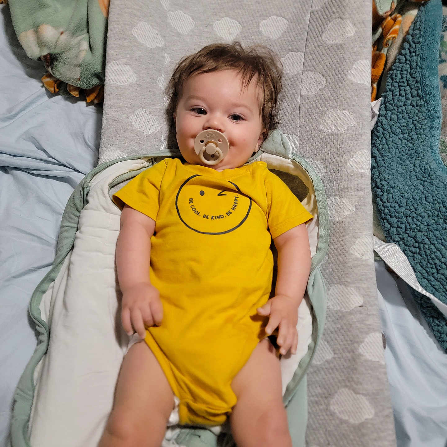 Leonard is registered to the contest to win money with this photo: baby, child, pacifier, yellow_onesie, changing_pad, blanket, bed, infant, cute, smiling, soft_lighting, indoors, resting, clothing, person, baby_bedding, portrait, comfort, happy, toddler