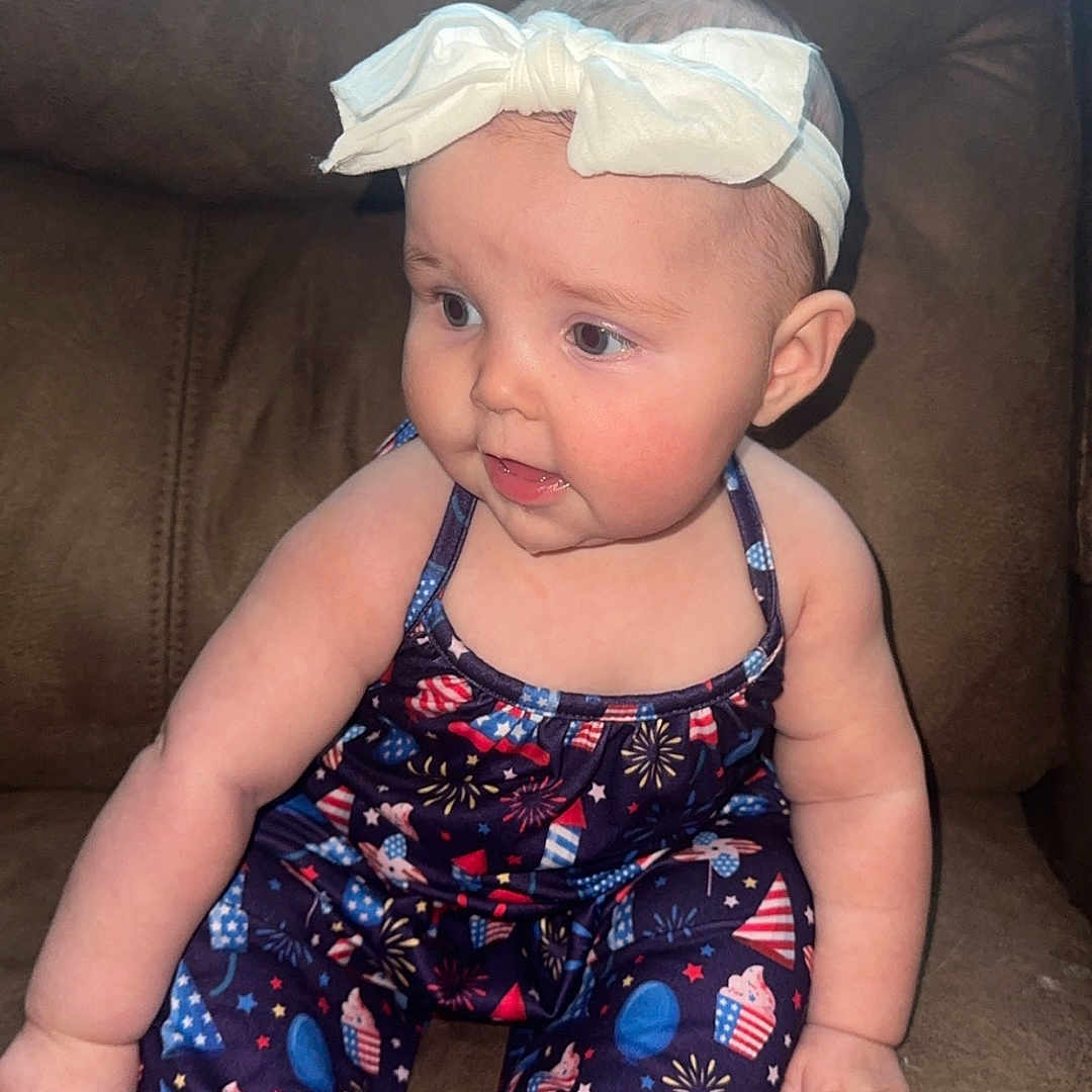 Sage is registered to the contest to win money with this photo: baby, baseballcap, bodypart, cap, clothing, couch, cushion, dress, face, finger, furniture, hat, head, homedecor, pants, person, photography, portrait, shorts, sitting