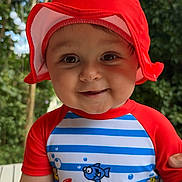 Zakaria a rejoint le concours — aidez-le/la à gagner de superbes lots ! baby, child, red_hat, swimsuit, striped_clothing, outdoor, smile, face, cute, sun_hat, cartoon_print, baby_clothing, greenery, summer, portrait, happy, headwear, infant, nature, daylight