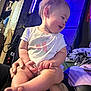 baby, child, person, indoor, purple_light, candid, smile, toddler, short_sleeve_shirt, bare_legs, hands, feet, adult_hand, seated, clothing, wall, furniture, casual, curly_hair, happy