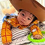 Esteban joined the competition — help win amazing prizes! baby, child, cowboy_hat, costume, yellow_shirt, toy, green_ring, blanket, soft_toys, indoor, portrait, cute, infant, face, hands, expression, striped_pillow, playtime, closeup, lying_down