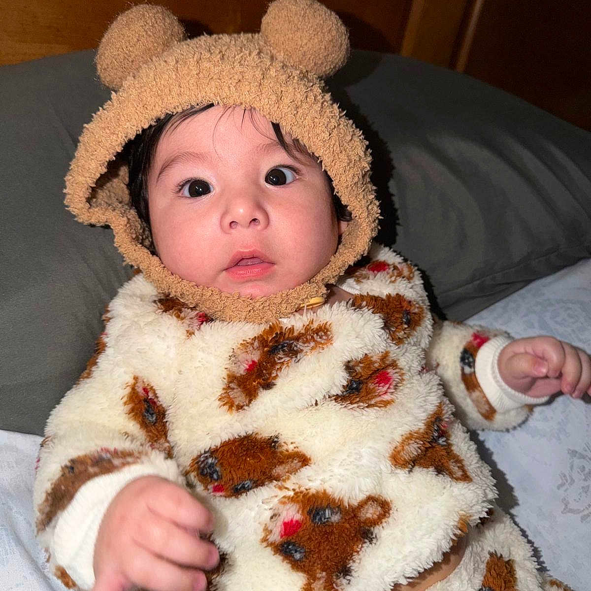 Esteban is registered to the contest to win money with this photo: baby, bear_pattern, bed, blanket, child, cozy, curious, cute, face, fuzzy_clothing, hand, hat_with_ears, indoor, infant, portrait, sleepwear, soft_texture, warm_clothing, wide_eyes, wooden_background