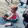 Lakelynn is registered to the contest to win money with this photo: baby, child, sitting, sandal, baby_bottle, outdoor, deck, wooden_floor, rug, patterned_rug, curious, looking_up, furniture, chair_leg, footwear, clothing, pink_top, blue_skirt, infant, portrait
