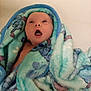 baby, blanket, blue, green, cartoon, face, infant, looking_up, open_mouth, wrapped, snug, soft, cute, child, newborn, expression, indoors, warm, cozy, portrait