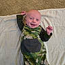 baby, infant, child, smiling, lying_down, portrait, face, camouflage, pajamas, blanket, bed, indoor, happy, arms_raised, fist, bald, looking_at_camera, close_up, cute, photography