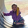 toddler, child, corn, purple_jacket, floral_pants, barefoot, smiling, outdoor, playground, pipe, grass, happy, sitting, person, nature, daylight, fun, holding, food, cute