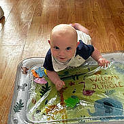 Theo is registered to the contest to win money with this photo: baby, infant, tummy_time, inflatable_mat, jungle_theme, animal_prints, wooden_floor, indoors, child, playtime, colorful, curious, smiling, cute, young_child, blue_shirt, bib, floor_play, giraffe, elephant